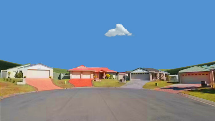 Empty suburban street with several houses and one small cloud in a clear blue sky, highlighting empty spaces unsettling appeal.