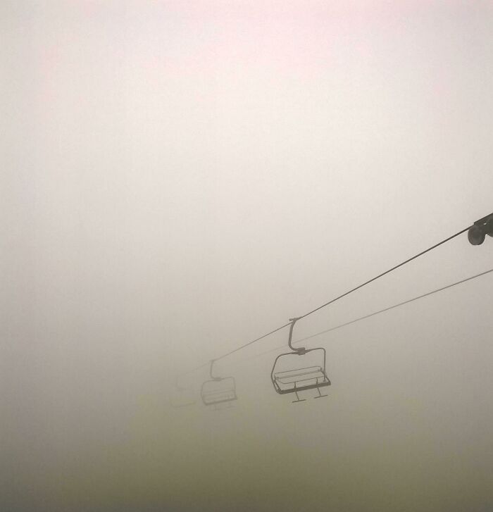 Empty ski lift chairs suspended in thick fog showing unsettling yet fascinating empty spaces.