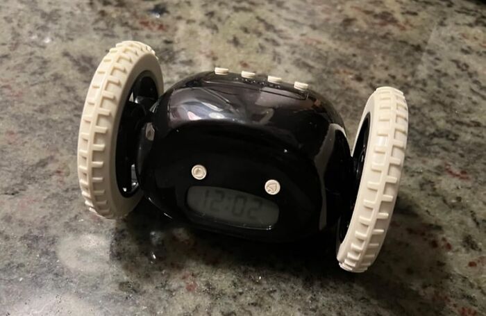 Black digital alarm clock with wheels on granite countertop, illustrating ways to hack your way into becoming a morning person.