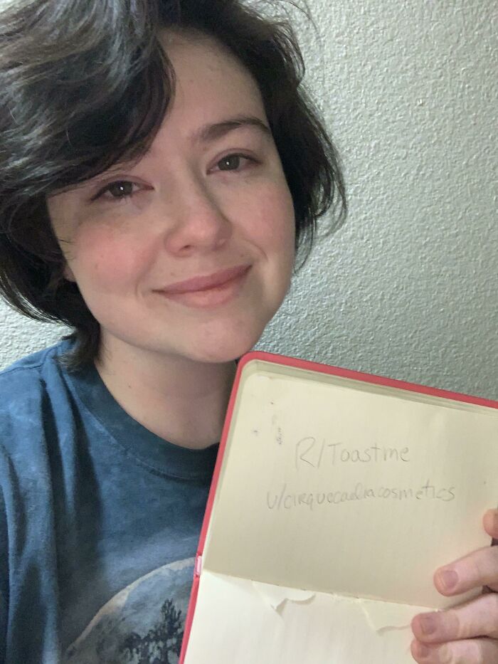 Young person smiling softly and holding a notebook with a toast request in a casual indoor setting for internet toast comments.