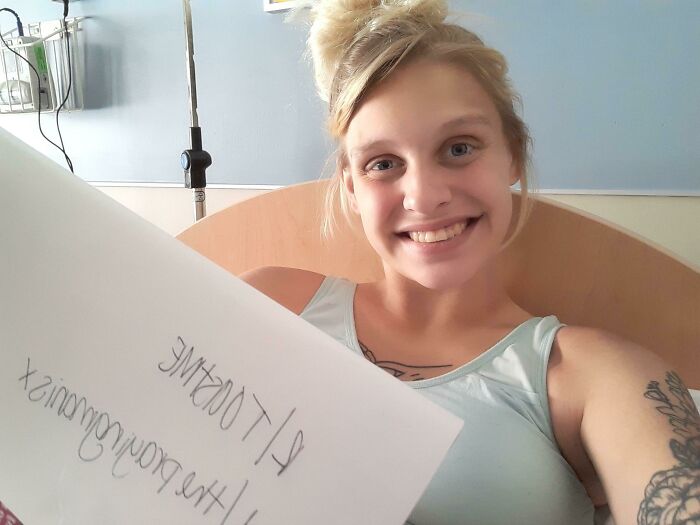 Young woman smiling in a hospital bed holding a sign, part of people who asked the internet to toast them series.