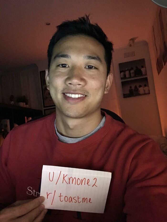 Young man holding a toastme sign, smiling warmly in a cozy indoor setting, capturing the spirit of internet toasting.