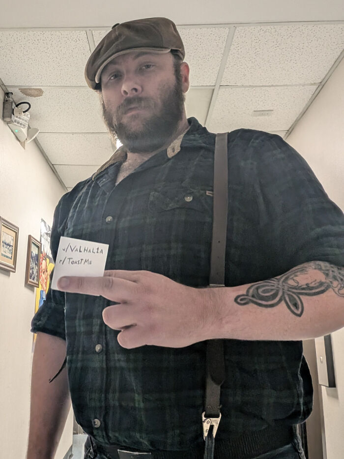 Man in plaid shirt and flat cap holding a note, part of 80 people who asked the internet to toast them collection.