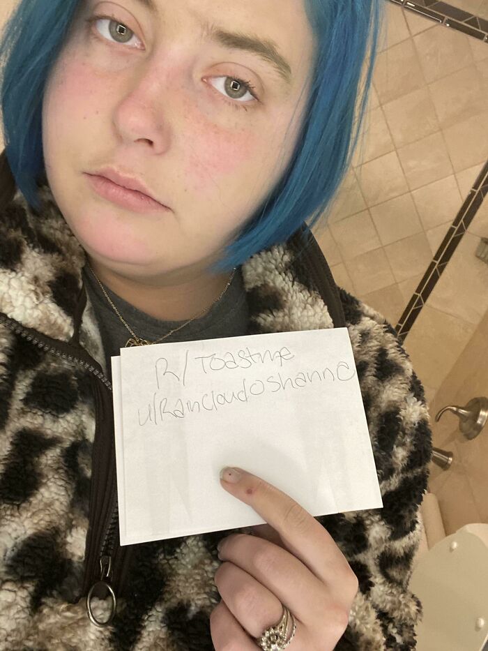 Person with blue hair holding a handwritten note in a bathroom, part of a collection of people who asked for internet toasts.