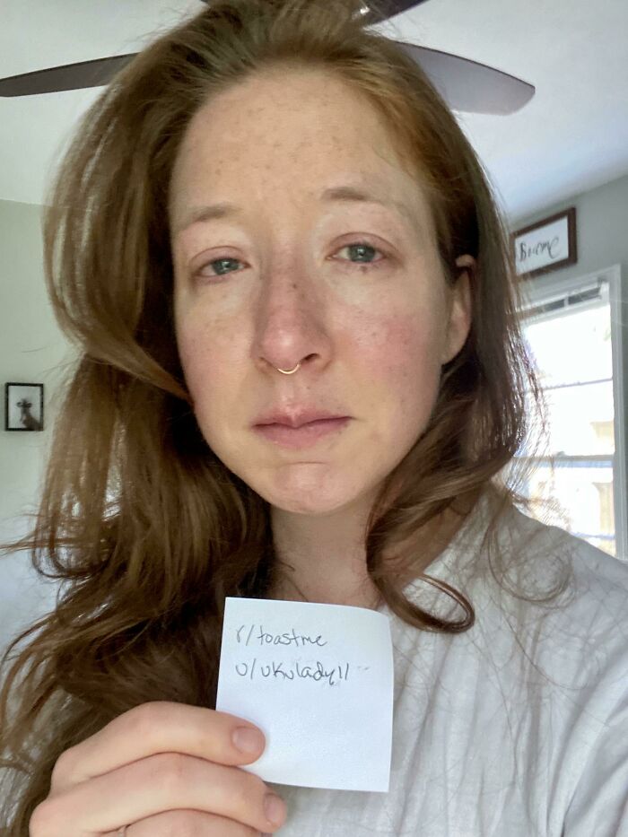 A woman with red hair in a white shirt holding a note, part of internet toast and nicest comments community.
