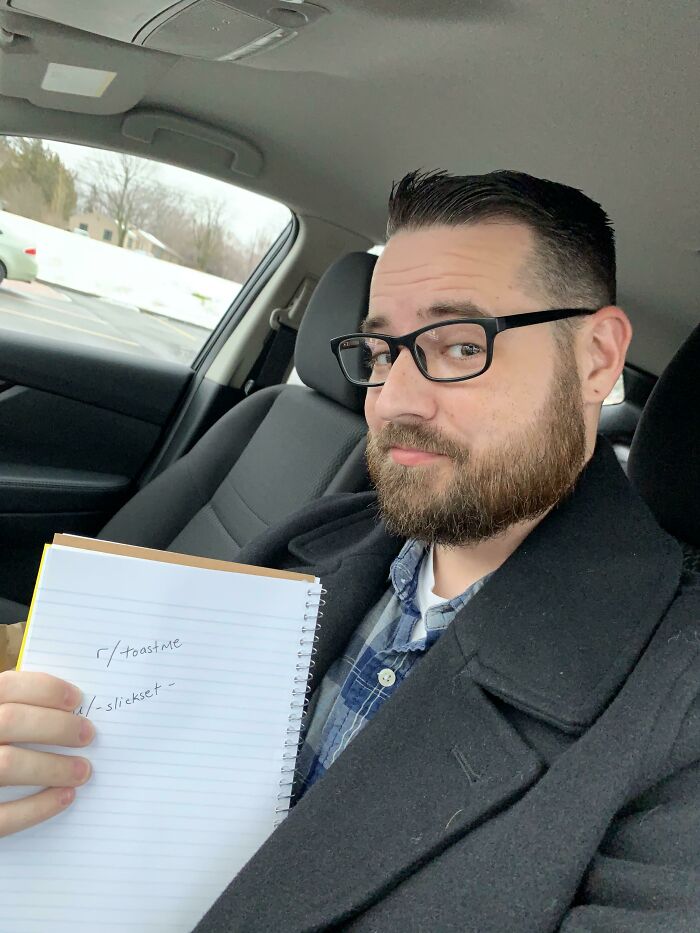 Man with glasses and beard sitting in a car holding a notebook, part of people who asked the internet to toast them collection.