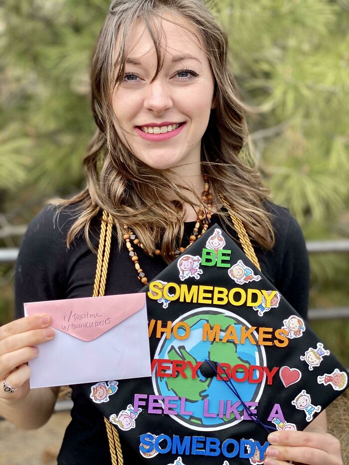 Young woman smiling outdoors holding a decorated graduation cap and an envelope, illustrating internet toast responses.