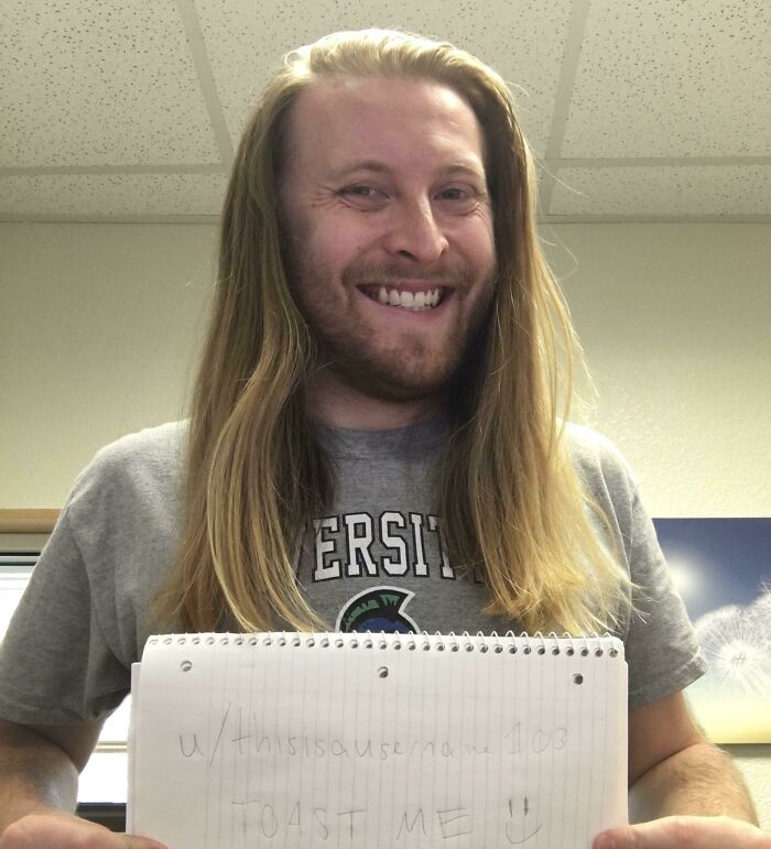 Smiling man with long hair holding a notebook asking the internet for a kind toast and positive comments.
