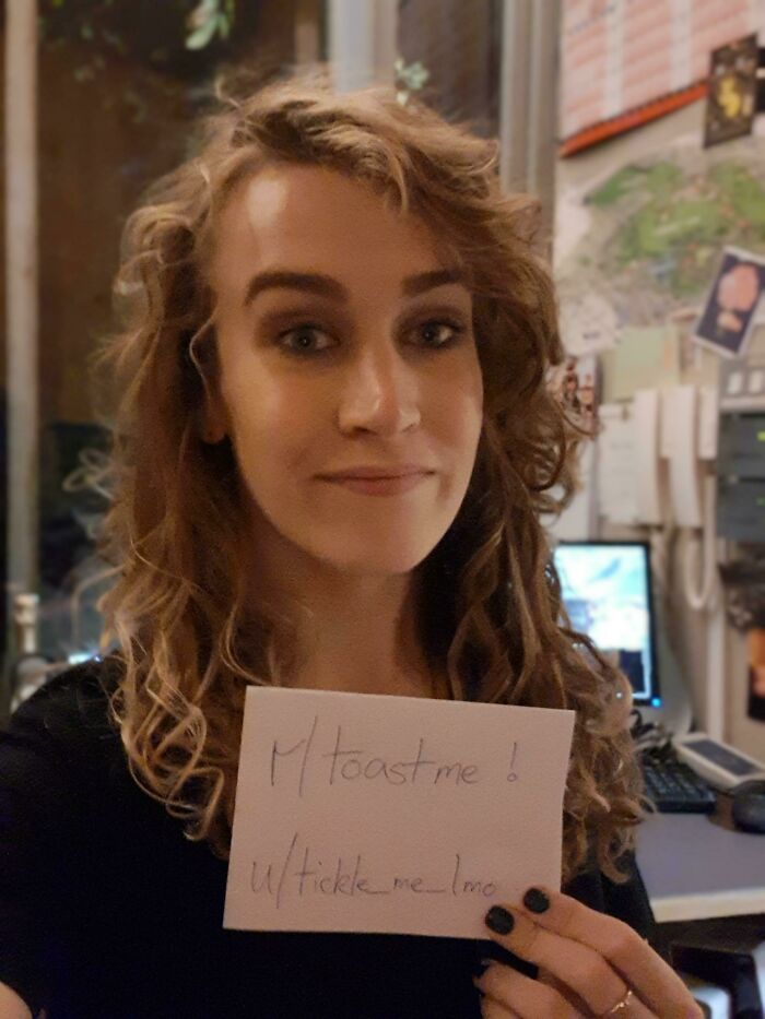 Person with curly hair holding a sign requesting to be toasted, representing people who asked the internet to toast them.