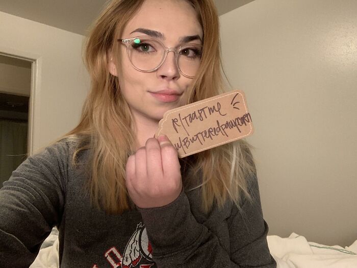 Young woman wearing glasses holding a sign asking for internet toast, smiling in a casual indoor setting.