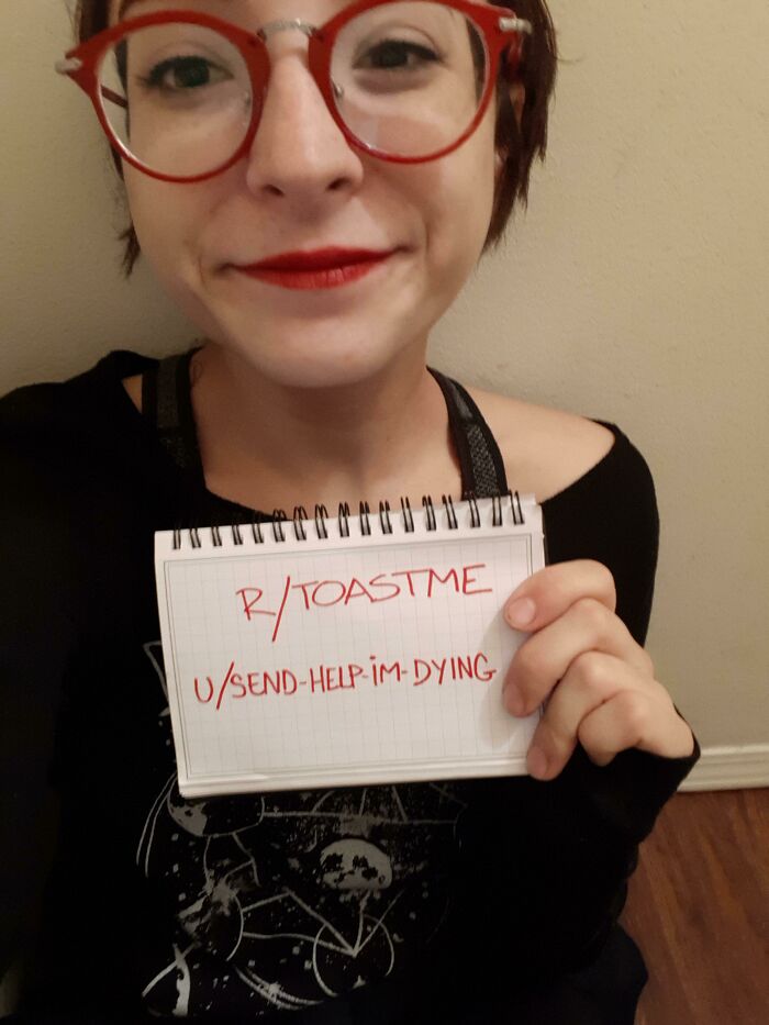 Young woman with red glasses smiling and holding a notebook with a toast me request for internet comments.