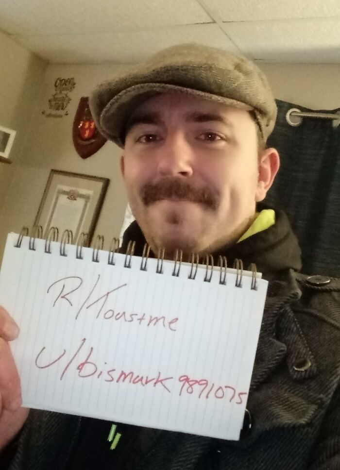 Man wearing a brown cap holding a notebook with reddit roastme sign, part of internet roast and toast comments trend.