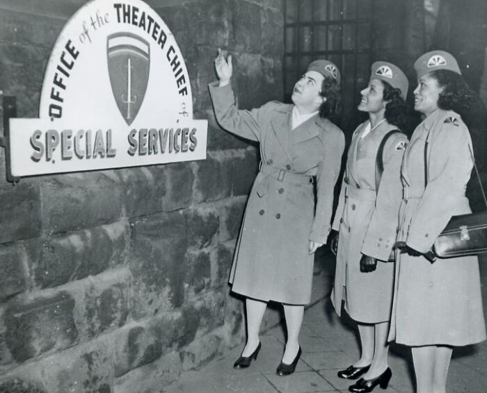 Three African American women in uniform stand at the Office of the Theater Chief of Special Services during wartime.