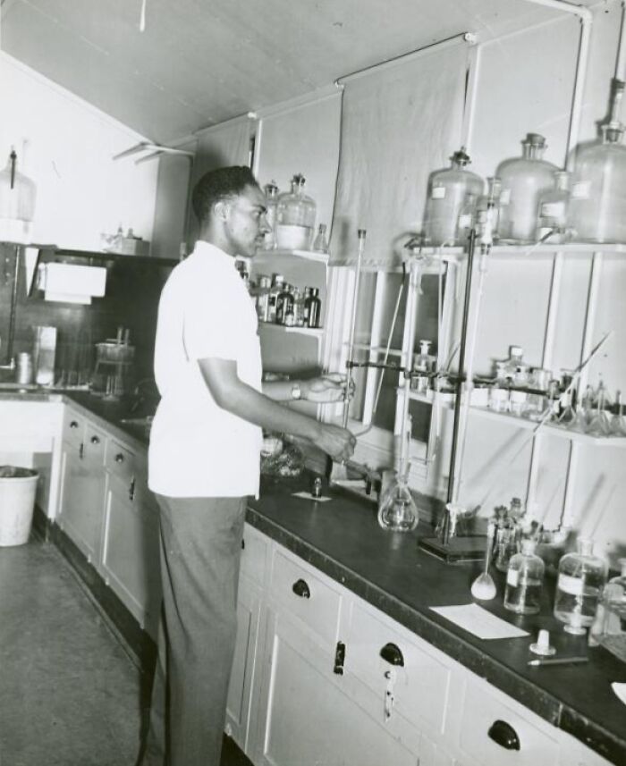 African American man in uniform working in a laboratory surrounded by glassware and scientific equipment.