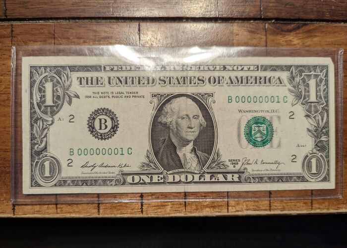 Rare one-in-a-million coincidence shown with a unique serial number one dollar bill preserved in plastic on wooden surface.