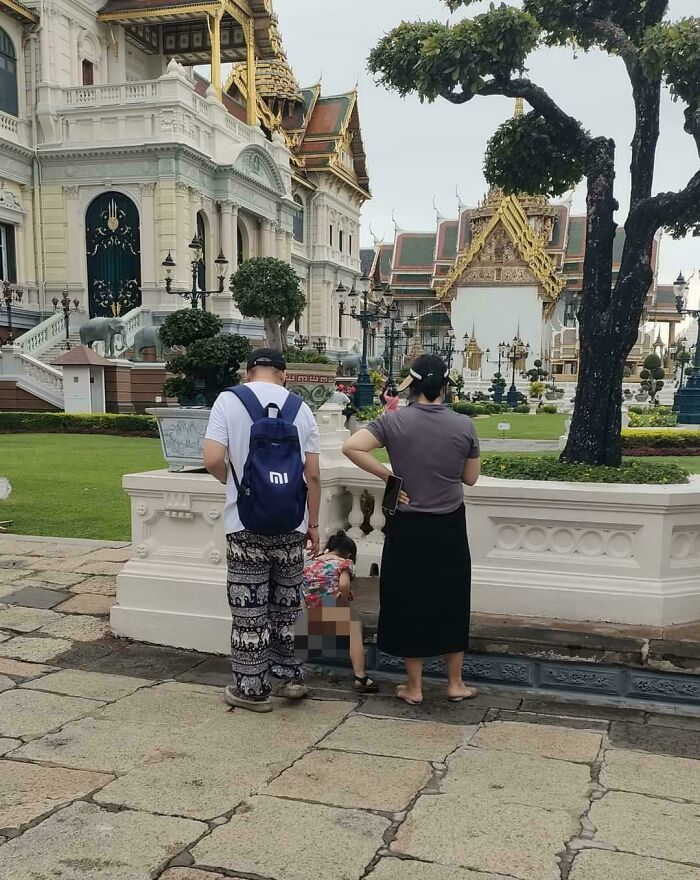 Entitled tourists with a child causing disruption in front of a historical temple with ornate architecture and gardens.