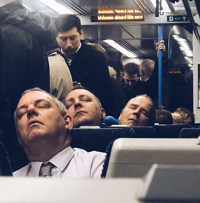Three men with similar facial expressions sleeping in a row on a crowded train, illustrating one-in-a-million coincidences.