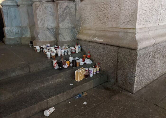 Empty cups and trash left on city stone steps by rude and entitled tourists, highlighting obnoxious tourist behavior and littering.