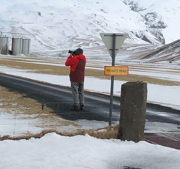 Tourist on a private road taking photos in a snowy mountainous area, showcasing entitled and rude tourist behavior.