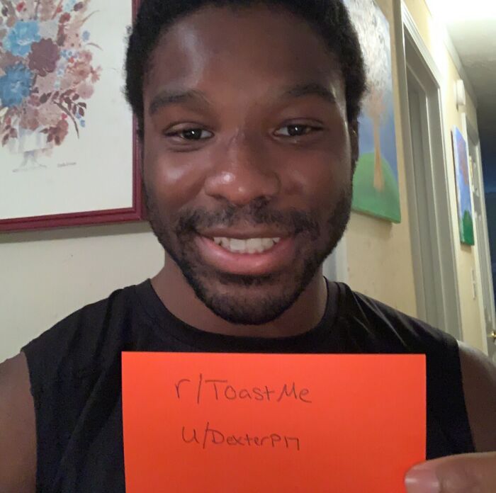 Smiling man holding a sign in a home setting, part of the internet toast challenge receiving nice comments.