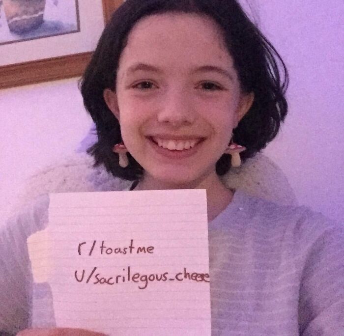 Smiling young person holding a note with their Reddit username, participating in an internet toast request.