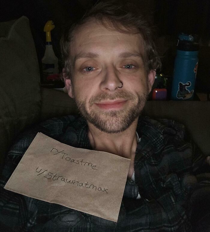 Man holding a toastme sign smiling softly in dim light, part of 80 people who asked the internet to toast them online.