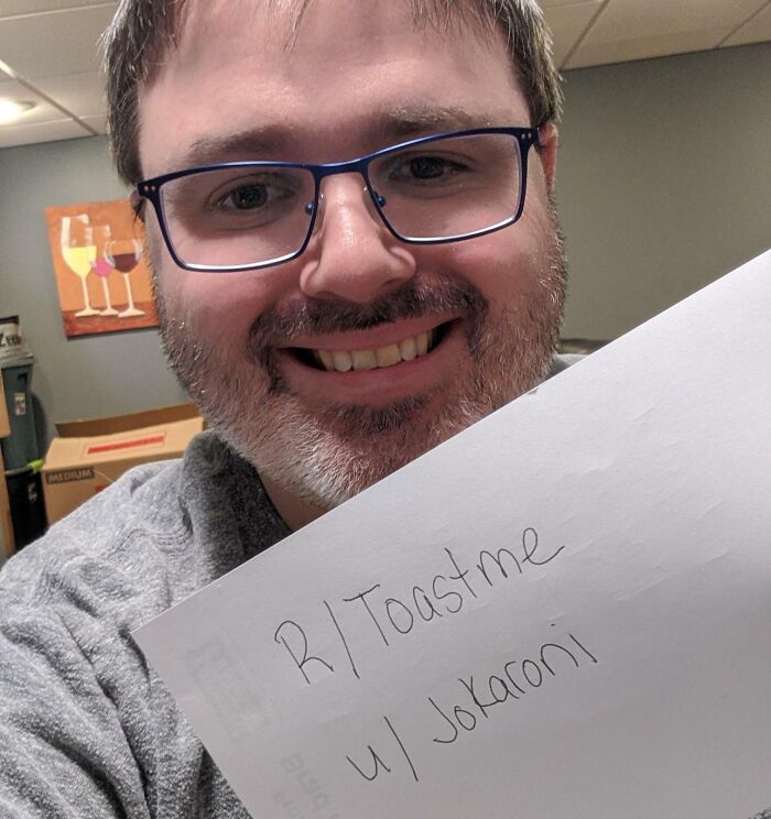 Man with glasses smiling and holding a paper, sharing a message requesting a toast and receiving kind comments online.