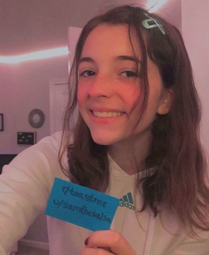 Young woman smiling while holding a toast request sign, receiving the nicest internet comments and positive support.