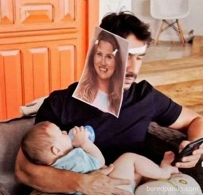 Man holding a baby bottle-feeding while looking at a phone, wearing a face shield with a woman's smiling face, dad humor meme.