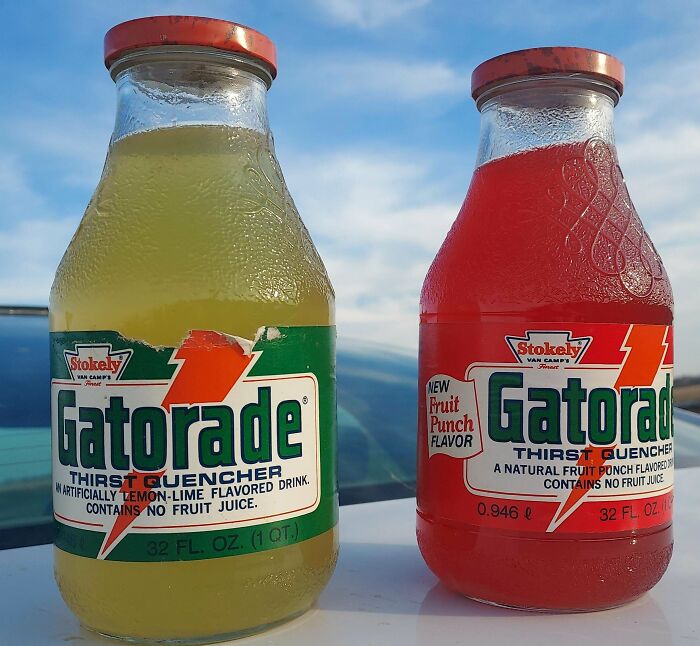Two vintage glass Gatorade bottles with lemon-lime and fruit punch flavors on a balcony with water and hills behind.