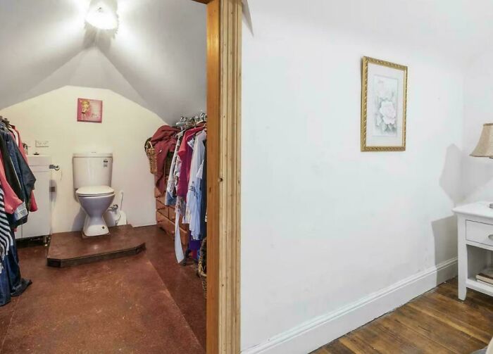 Small bathroom with toilet placed awkwardly next to clothes in a cramped rental space showing bad landlords' poor design.
