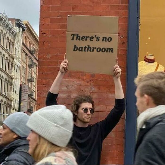 Man wearing sunglasses holding cardboard sign saying theres no bathroom, highlighting bad landlords making renting a nightmare