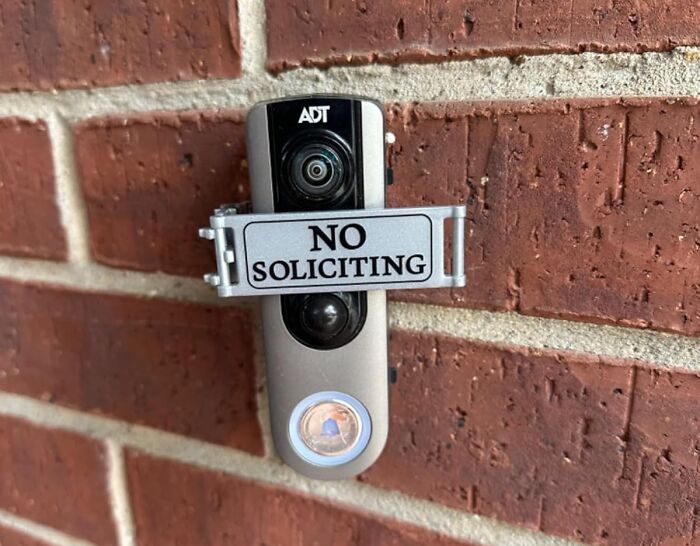 Security camera with no soliciting sign attached, mounted on a red brick wall, capturing hidden gems on Amazon.