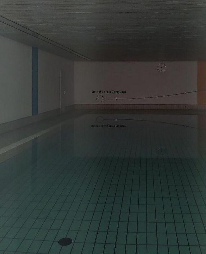 Dimly lit empty indoor pool with calm water, capturing the unsettling yet fascinating atmosphere of empty spaces.