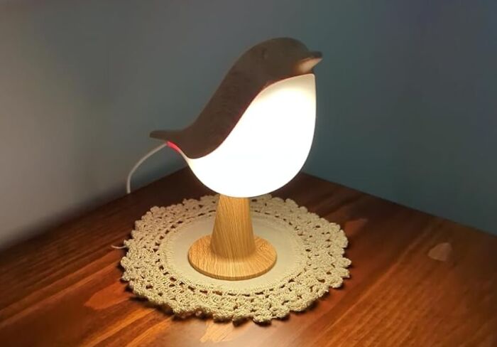 Bird-shaped lamp glowing softly on wooden table with crocheted doily in cozy room, popular TikTok finds.