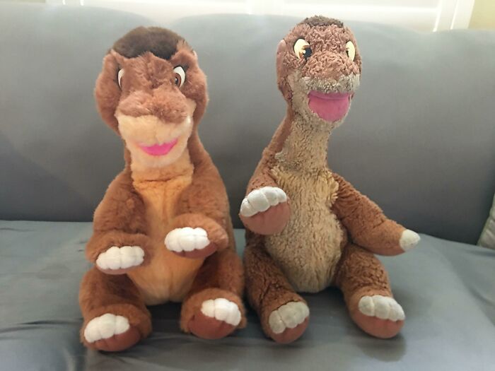Two dinosaur plush toys side by side showing before and after signs of wear and color change on a gray couch.