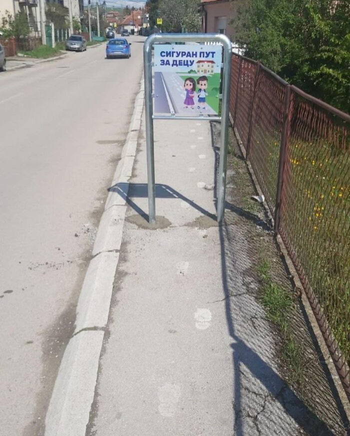 Metal signpost installed in the middle of a narrow sidewalk, illustrating dangerous designs and potential death traps.