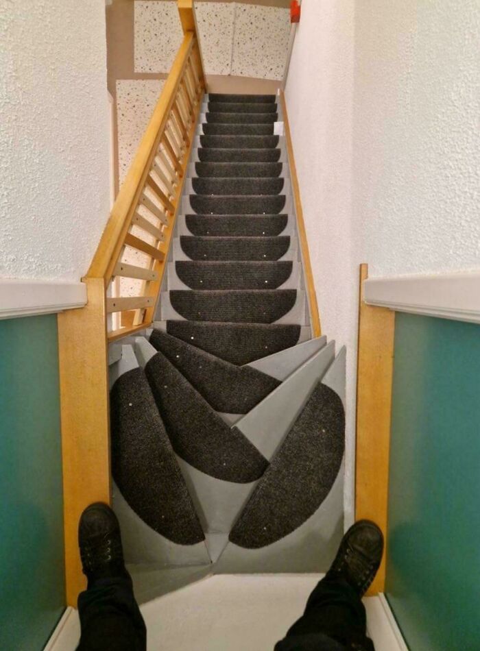 Steep narrow stairs with uneven, dangerously designed steps and dark carpet patches creating a hazardous visual effect.
