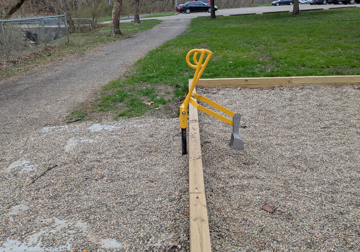 Playground digging toy with sharp metal parts placed over gravel and a wooden border, showcasing dangerous design features.