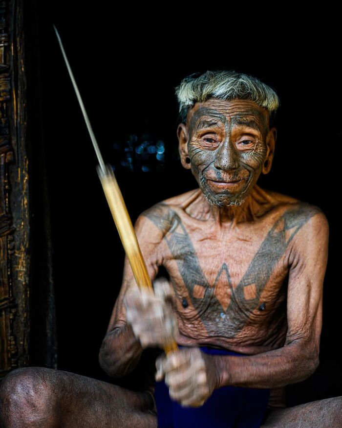 Elderly man with tribal tattoos holding a wooden spear, showcasing striking portrait of elderly people across the globe.