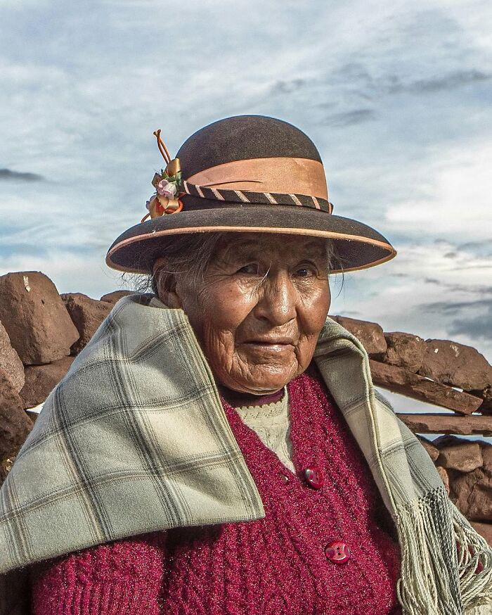 Elderly woman wearing a traditional hat and shawl in an outdoor setting, captured in striking portrait photography.