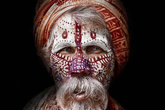 Elderly man with intricate face paint and traditional turban captured in a striking portrait by Massimo Bietti.