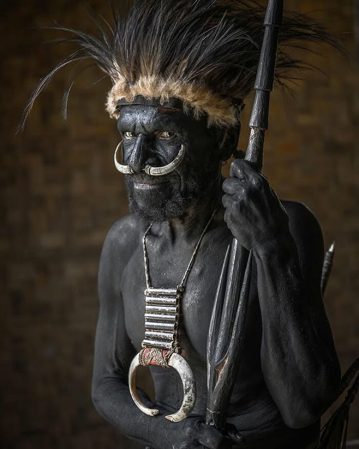 Elderly man with traditional face paint and tribal ornaments holding a spear in striking portrait by Massimo Bietti.