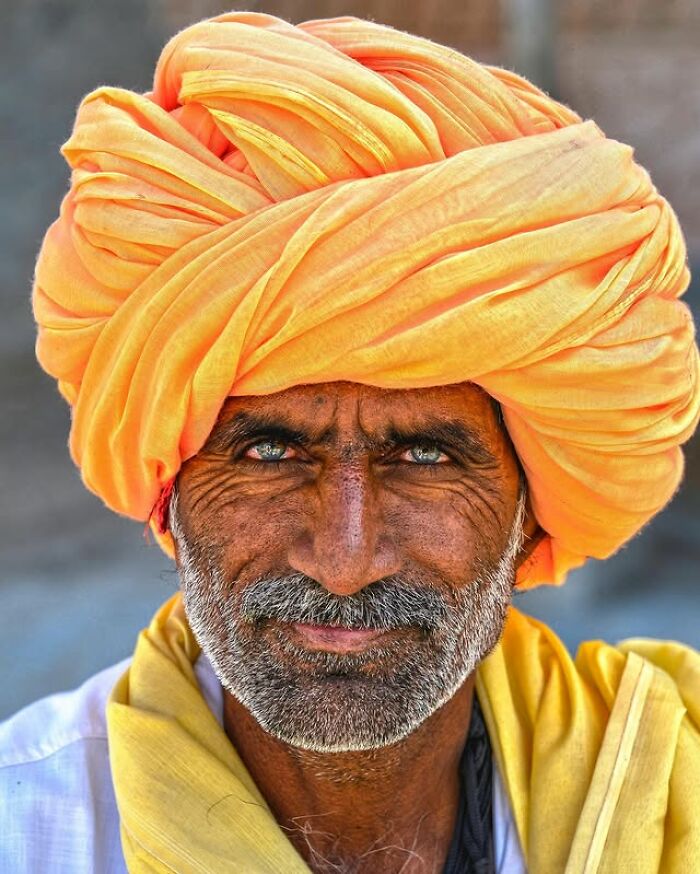 Elderly man with striking blue eyes wearing a bright orange turban in a portrait by Massimo Bietti.