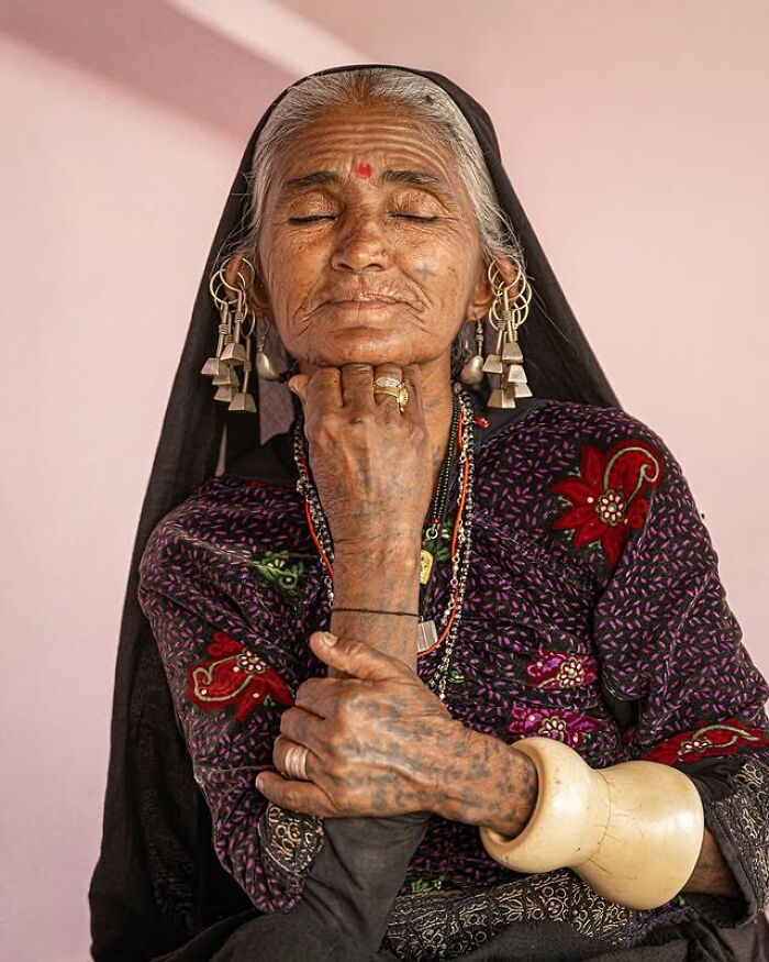 Elderly woman with traditional earrings and tattooed hands, captured in a striking portrait of elderly people across the globe.