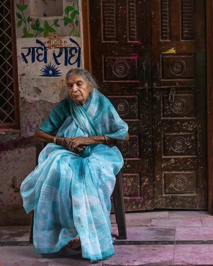 Elderly woman in a blue sari sitting peacefully, a striking portrait of elderly people captured by Massimo Bietti.