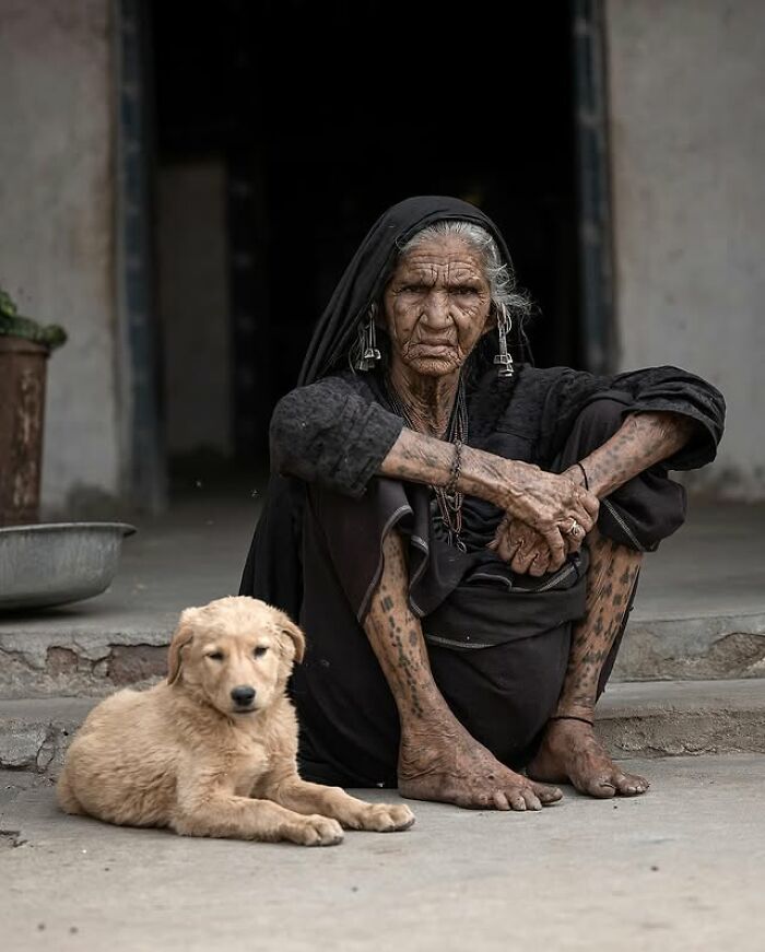 Elderly woman with traditional tattoos sitting beside a golden puppy in a striking portrait of elderly people.