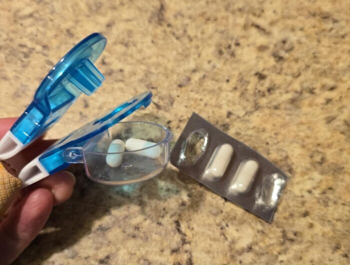 Hand holding blue pill cutter with white capsules and blister pack on a countertop showing bestsellers pandas are buying.