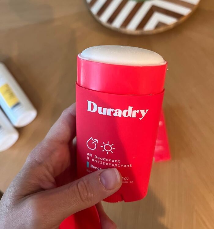Hand holding a red Duradry antiperspirant stick, a top summer body game-changer for sweat control.