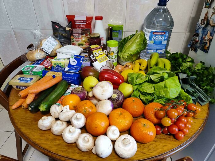 Various fresh fruits, vegetables, dairy, and packaged groceries displayed on a wooden table showing grocery costs.